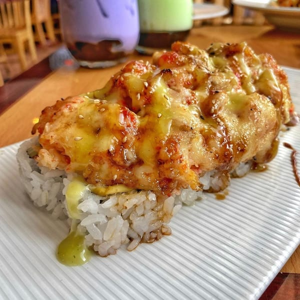 Tengoku Sushi's baked sushi roll, topped with melted cheese, sesame seeds, and a drizzle of sauce.
