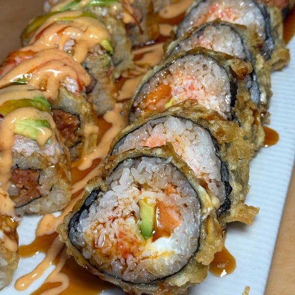 Close-up of crispy fried sushi rolls drizzled with a creamy orange sauce and avocado slices.