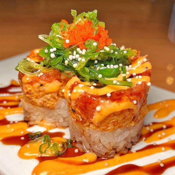 Two Tengoku Sushi rolls topped with seaweed salad, orange roe, and white sesame seeds.