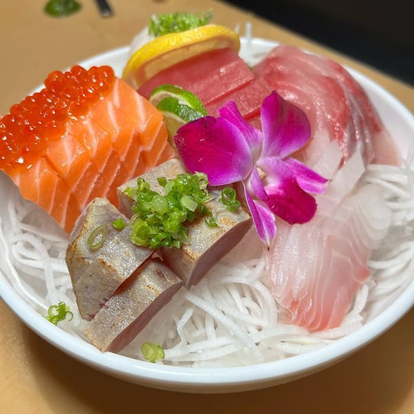 A colorful sashimi platter from Tengoku Sushi with salmon, tuna, and white fish, garnished with a purple orchid.