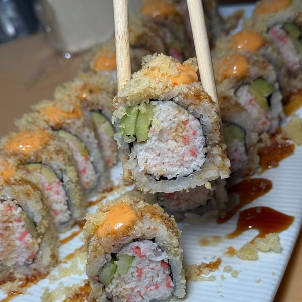 Chopsticks holding a piece of crispy sushi roll with avocado, crab, and spicy mayo.