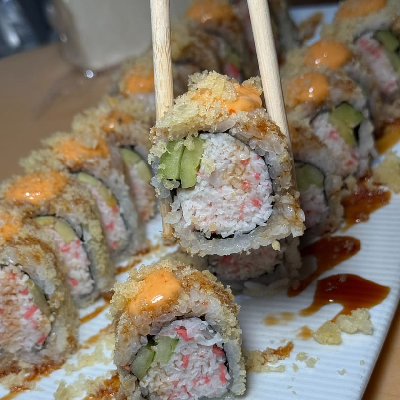 Chopsticks holding a piece of crispy sushi roll with avocado, crab, and spicy mayo.