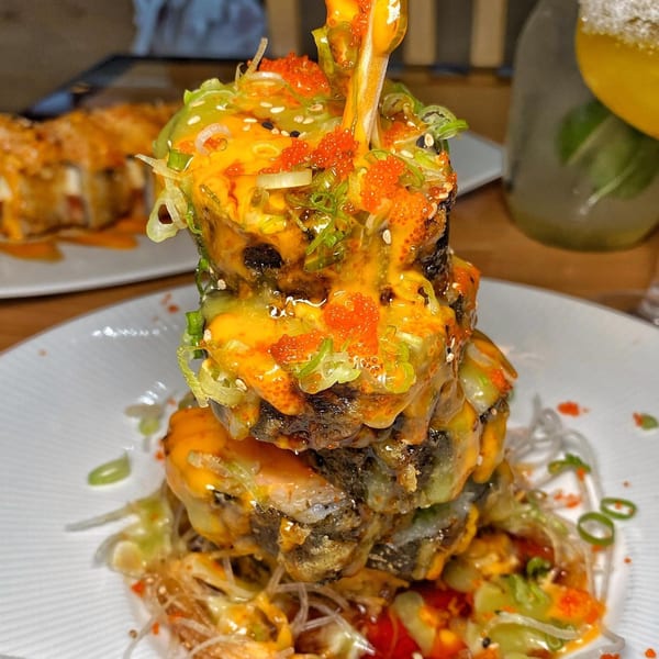 A towering stack of Tengoku Sushi rolls, drizzled with orange sauce, green onions, and tobiko.