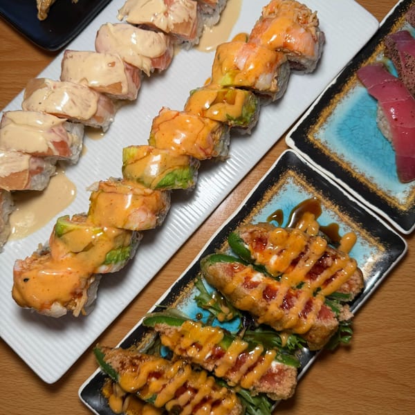 Plates of sushi rolls with creamy sauces, jalapeño poppers, and tuna nigiri on a wooden table.